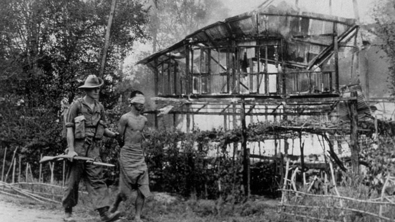 Британский солдат сопровождает японского пленного, когда вокруг них горит Бирма