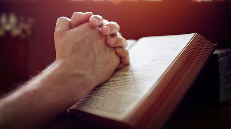 Руки мужчины сцеплены над открытой Библией.