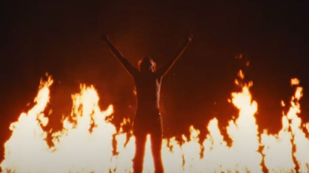 The young man Jeremy lifts his arms in front of fire in 