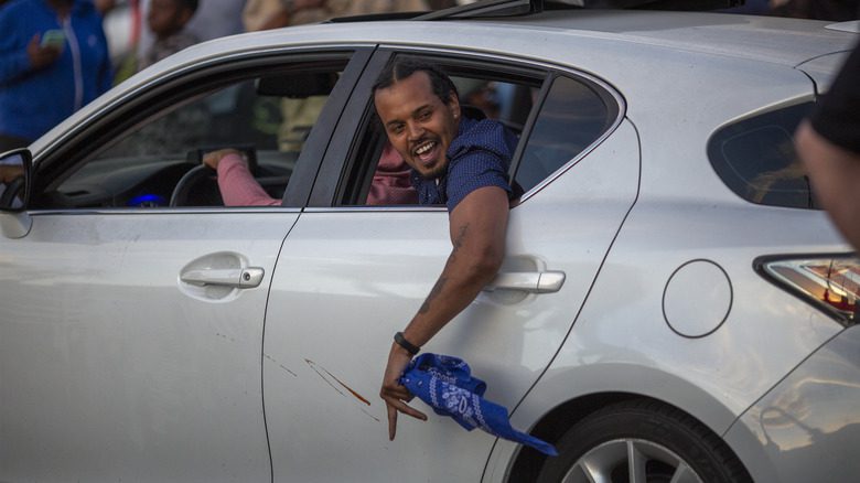 man waves blue bandana from car