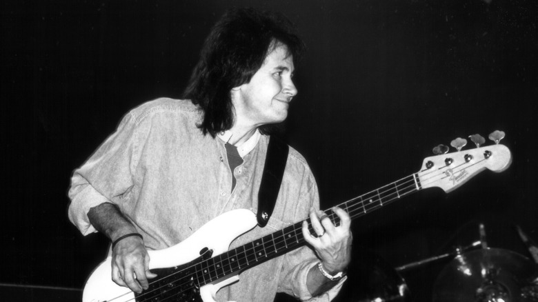 Джон Риган улыбается, играя на бас-гитаре на сцене