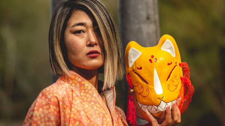 Азиатская женщина держит маску кицунэ