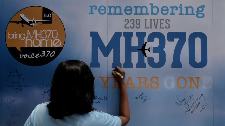 Женщина подписывает мемориальную стену рейса 370